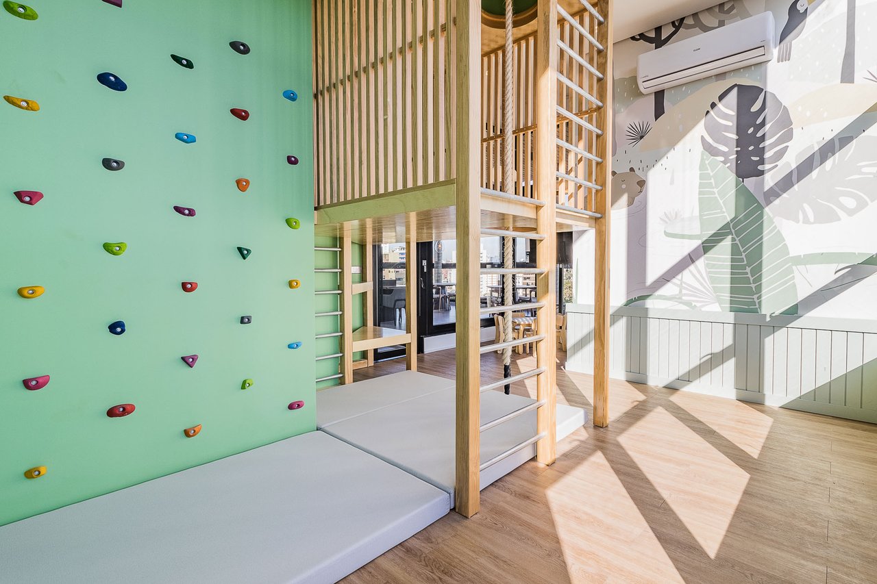 Espaço kids do Z800 com parede de escalada colorida, escada, corda e painel lúdico com estampa tropical