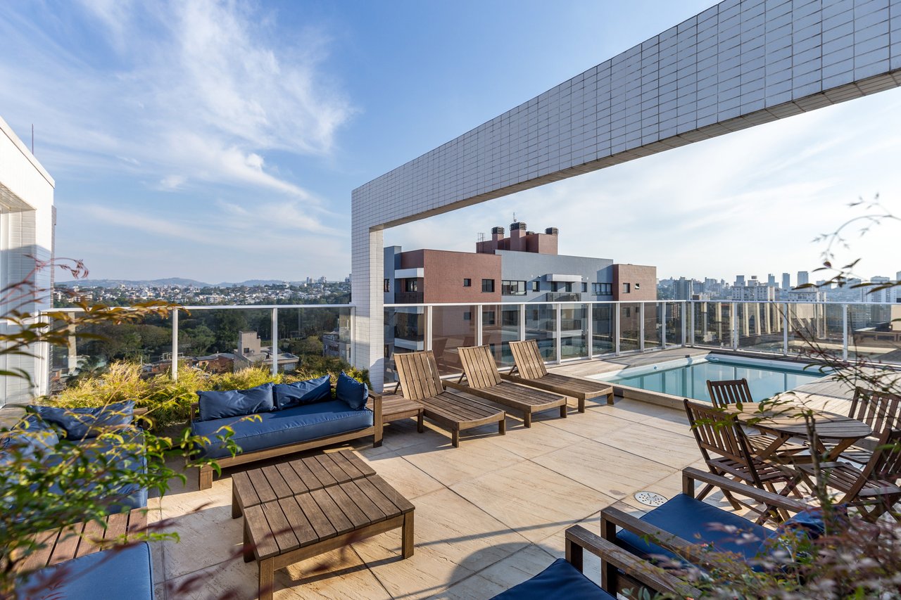 Rooftop do Sky com espreguiçadeiras de madeira, lounge azul e piscina com vista da cidade