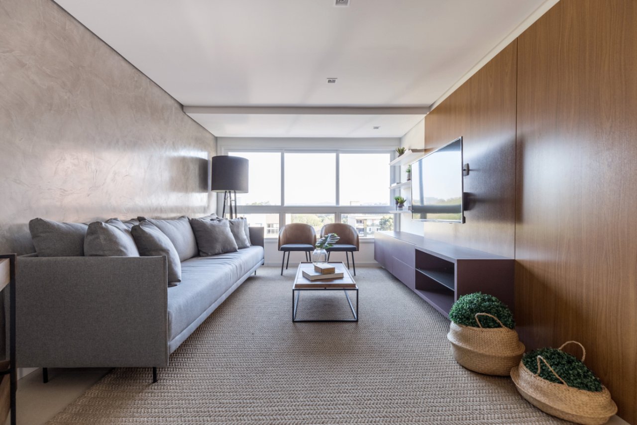 Living amplo do Sky com sofá cinza, painel de madeira e iluminação natural abundante