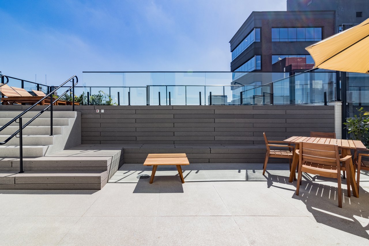 Deck do rooftop do Z800 com bancos, mesas em madeira, ombrelone e guarda-corpo em vidro