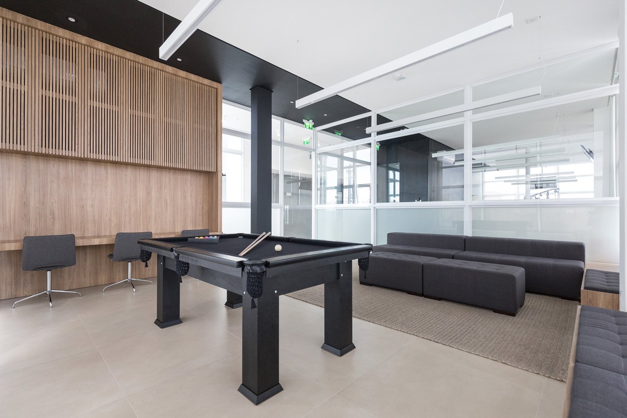 Sala de jogos do Sky com mesa de sinuca preta, lounge cinza e painel ripado de madeira