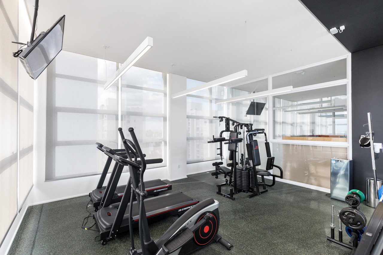 Espaço fitness do Sky com esteiras, elíptica e estação de musculação em frente a grandes janelas