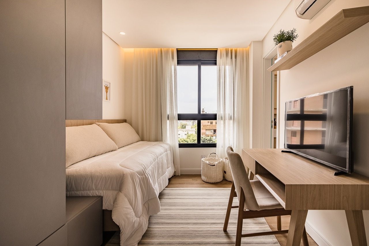 Dormitório do Z800 com escrivaninha, cama de solteiro e amplas esquadrias com vista externa