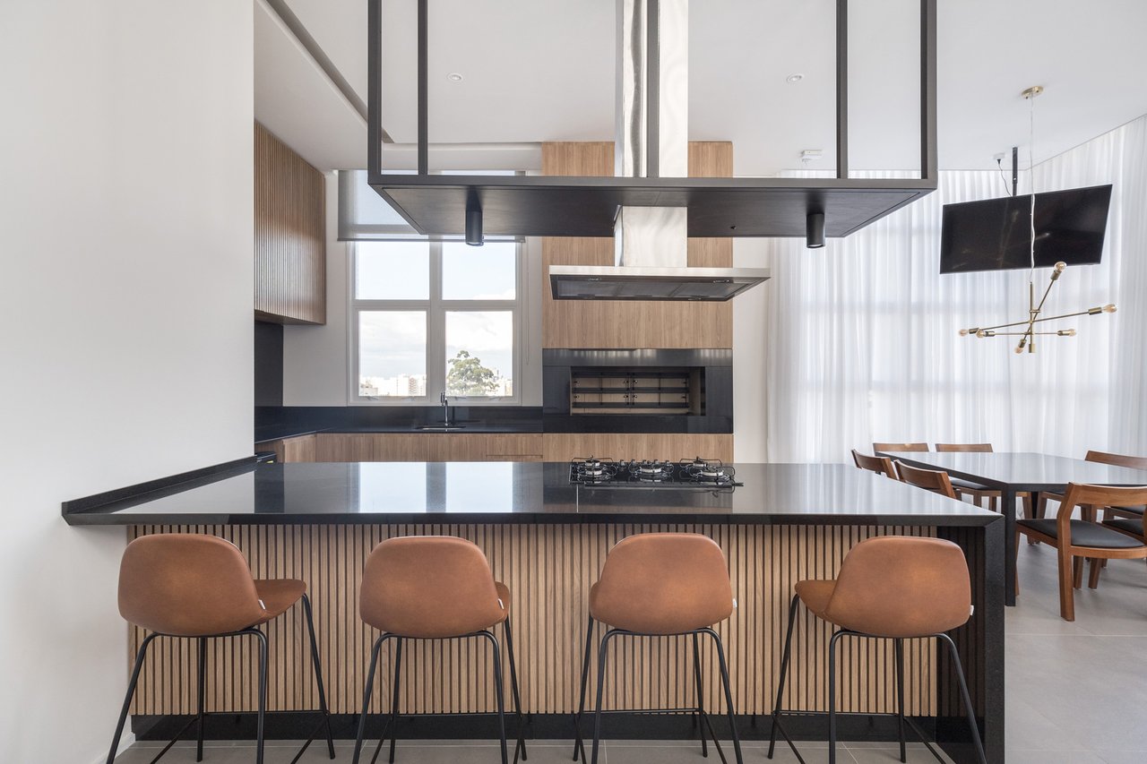 Espaço gourmet do Sky com ilha em granito preto, churrasqueira, cooktop e banquetas de couro caramelo