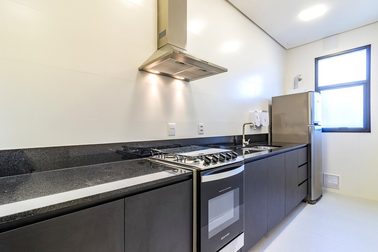 Cozinha do espaço gourmet do Z800 com bancada em granito escuro, cooktop, forno, coifa em inox e geladeira