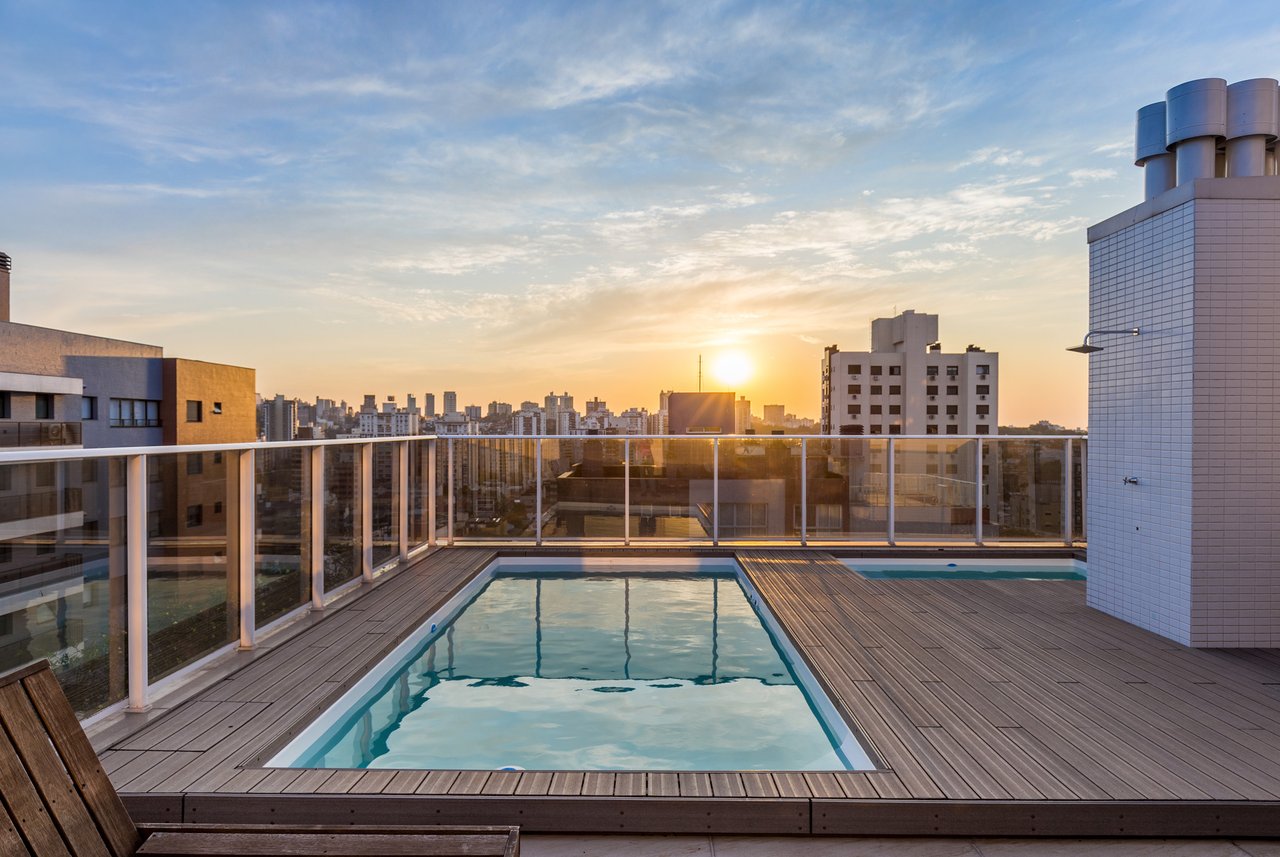 Piscina no rooftop do Sky com deck de madeira e pôr do sol sobre Porto Alegre